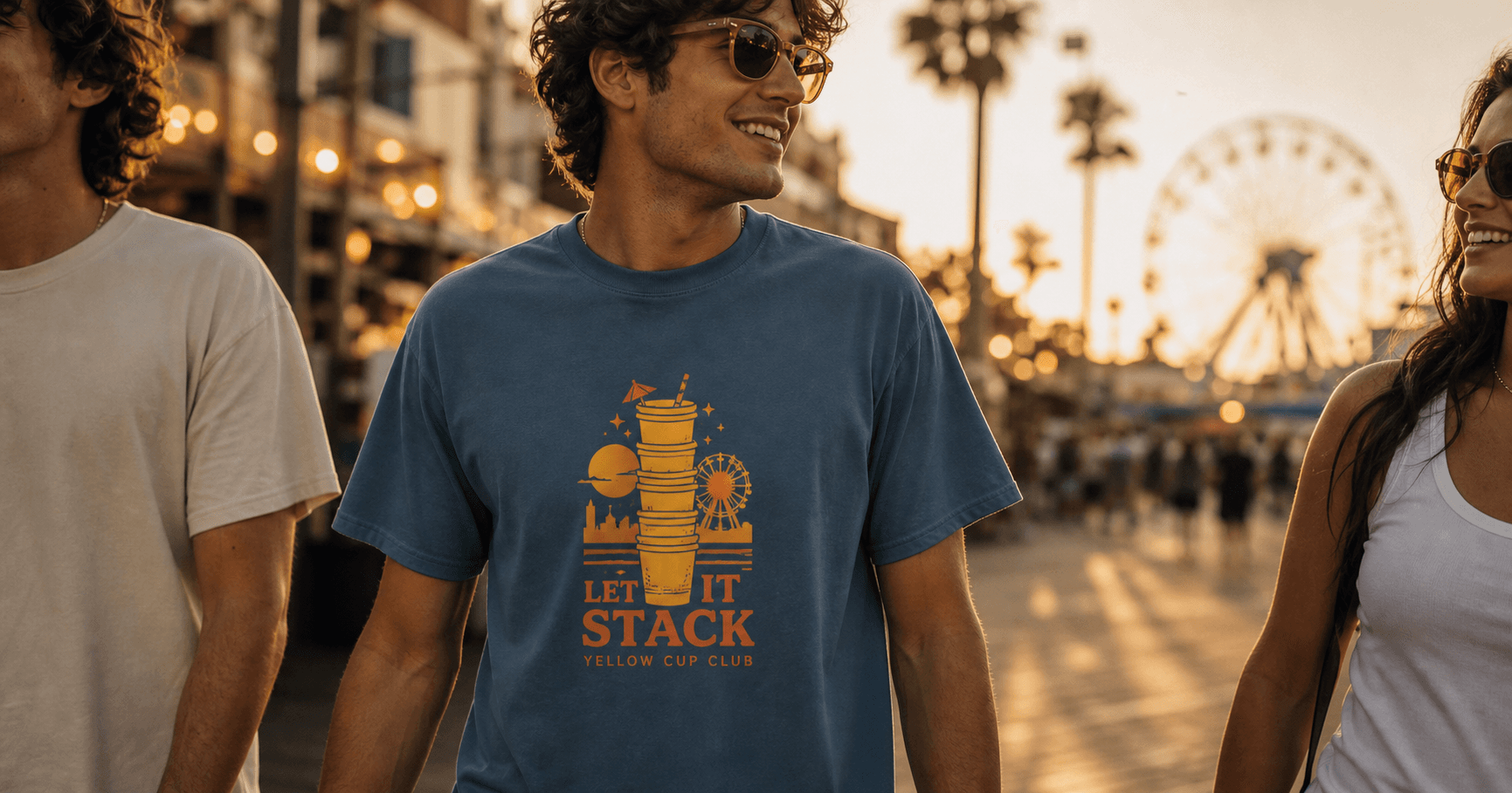 Model wearing a blue Not Necessarily Apparel graphic tee on a sunset promenade